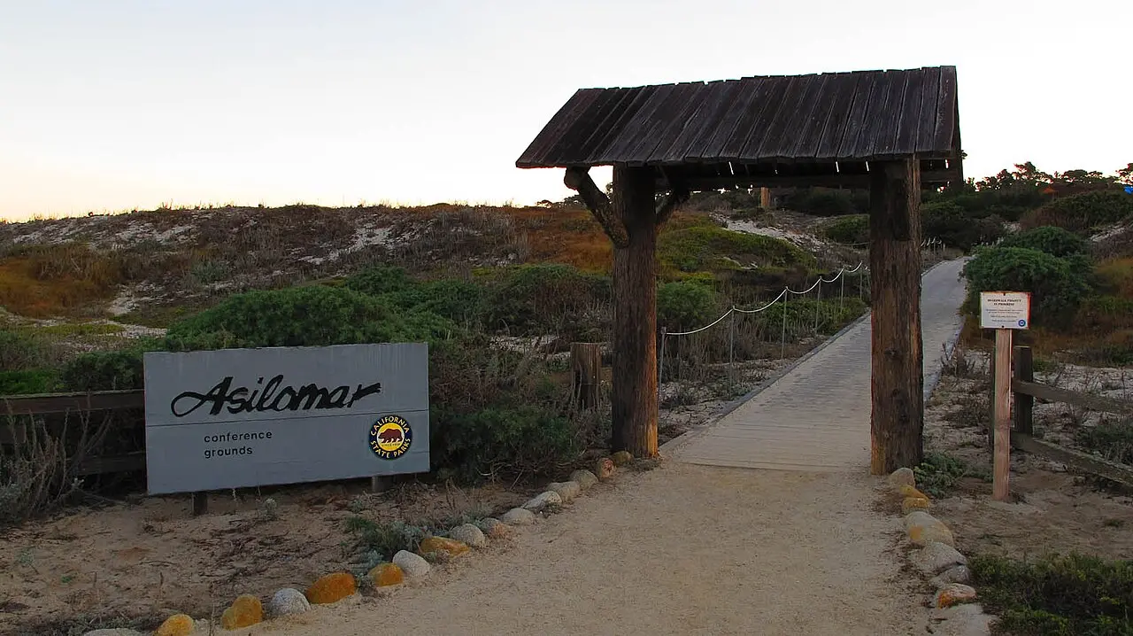カリフォルニア州パシフィックグローブのアシロマ会議場（Asilomar conference grounds）の看板と、海岸の砂丘へ続く木造の門