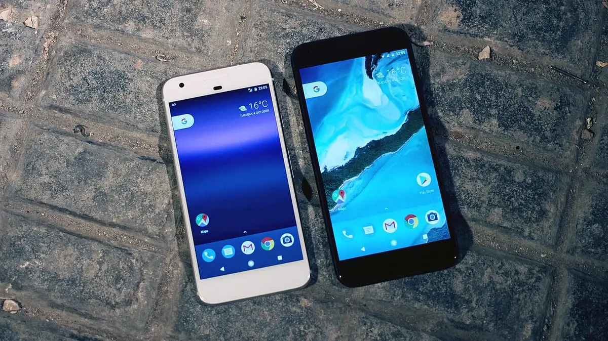 A white first-generation Google Pixel and a black Pixel XL on paving stones, their screens showing the date 4 October