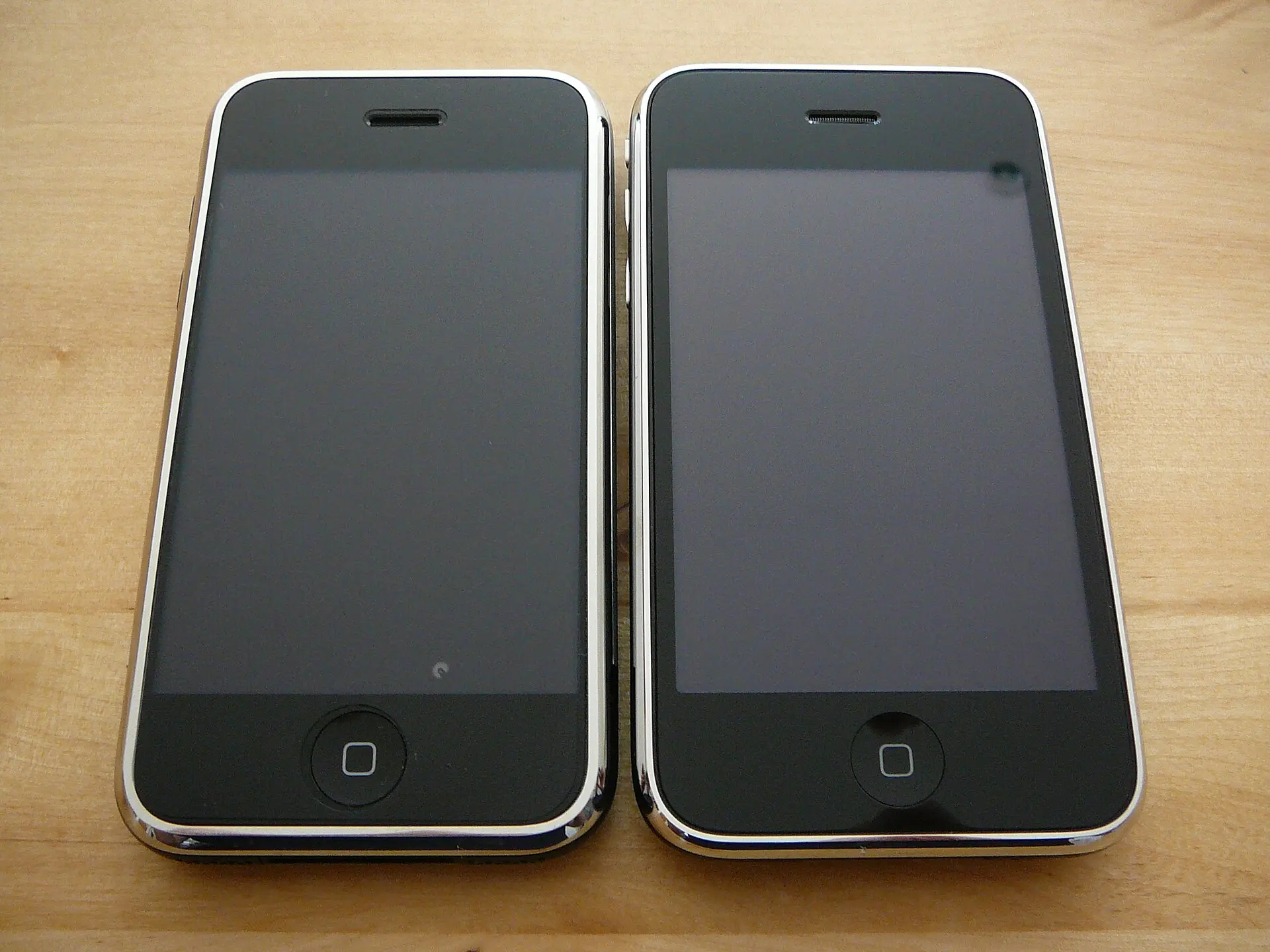 木製の机に並べて置かれた初代 iPhone（左）と iPhone 3G（右）の前面。2008年7月11日の発売日に撮影
