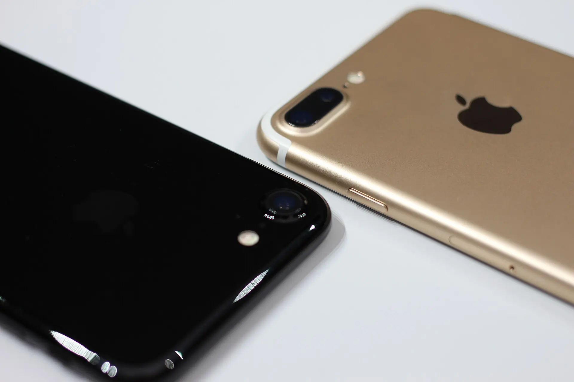 Close-up of the backs of a jet-black iPhone 7 (left) and a gold iPhone 7 Plus (right), the Plus carrying its two rear cameras