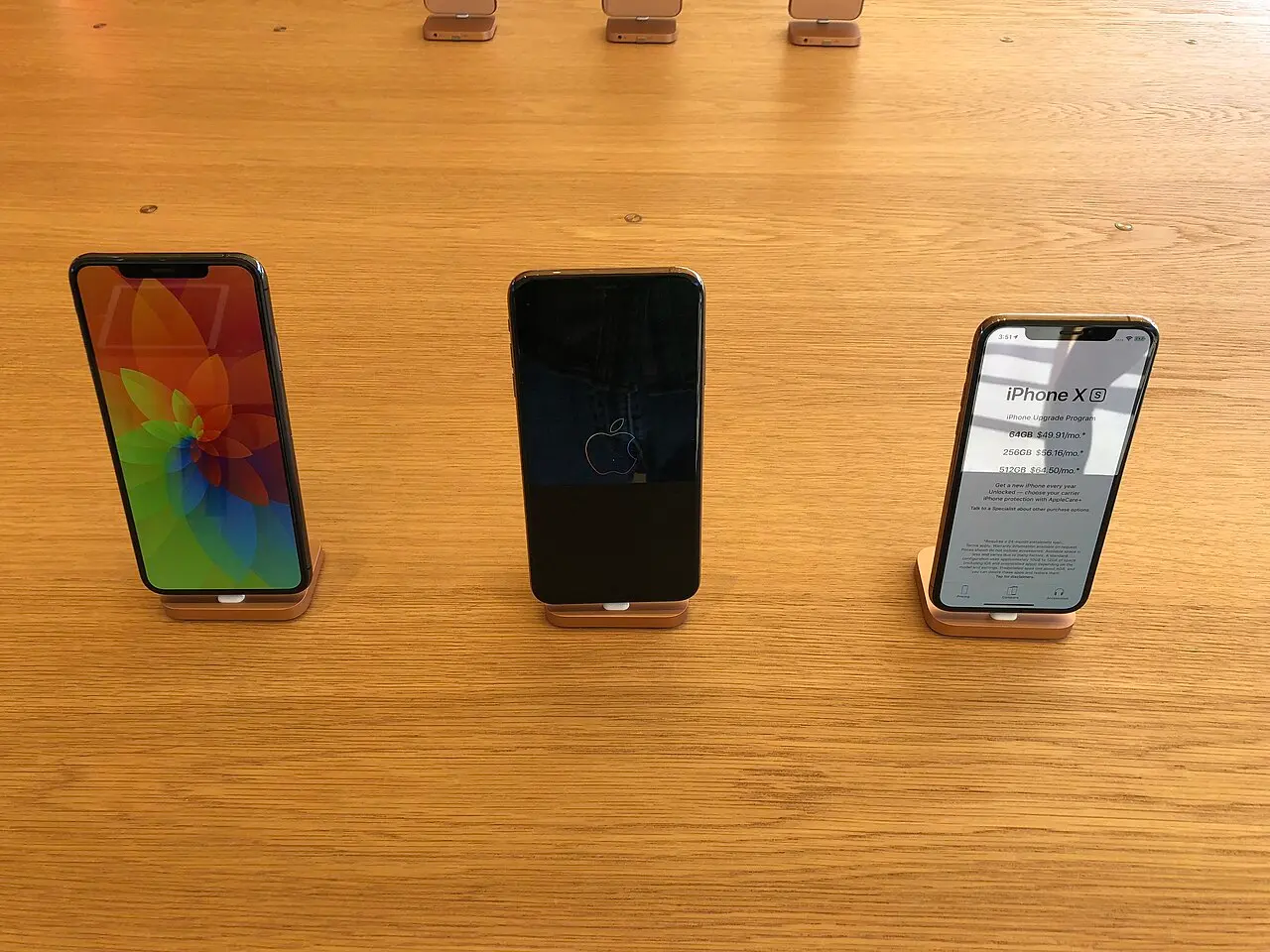 Three notched iPhone XS units on display on a wooden Apple Store table
