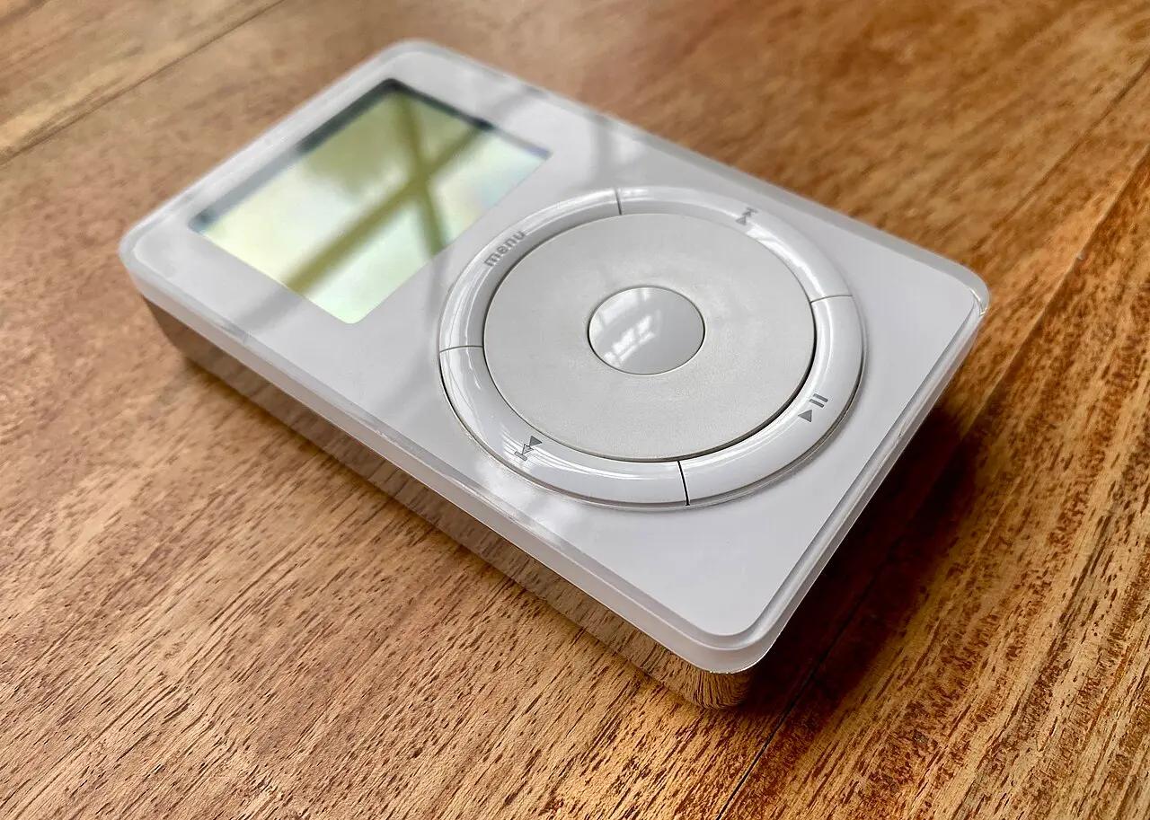 A first-generation iPod on a wooden table, showing its monochrome screen and scroll wheel