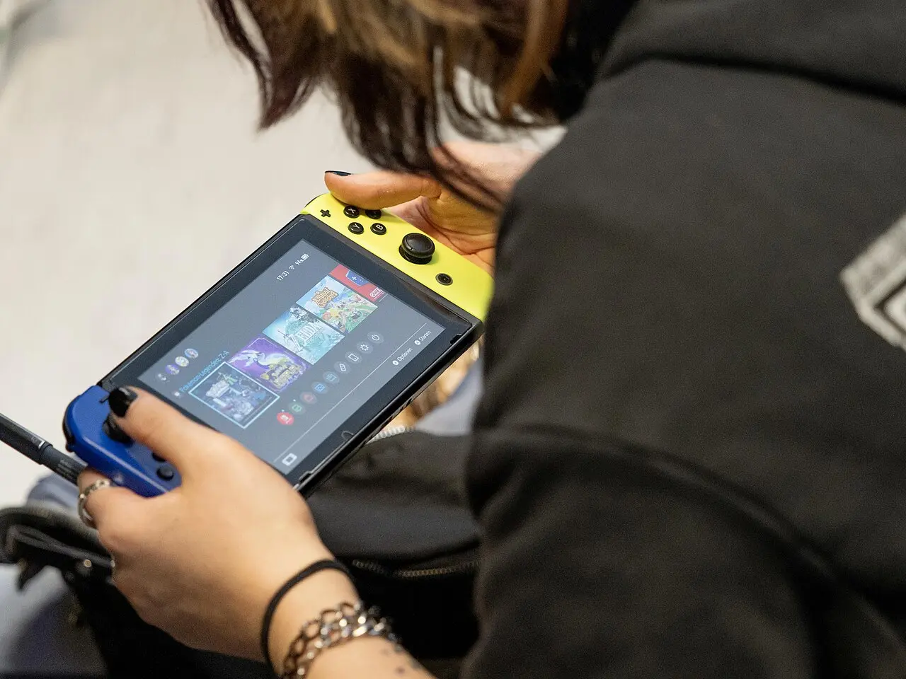 A person holding a Nintendo Switch in handheld mode, selecting a game from the home menu