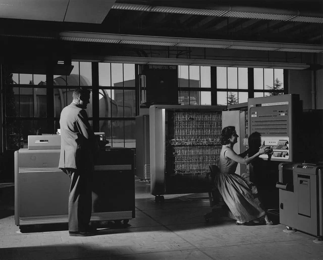 An IBM 704 at NASA Ames Research Center in October 1958, with a woman operating the console and a man standing at a card unit