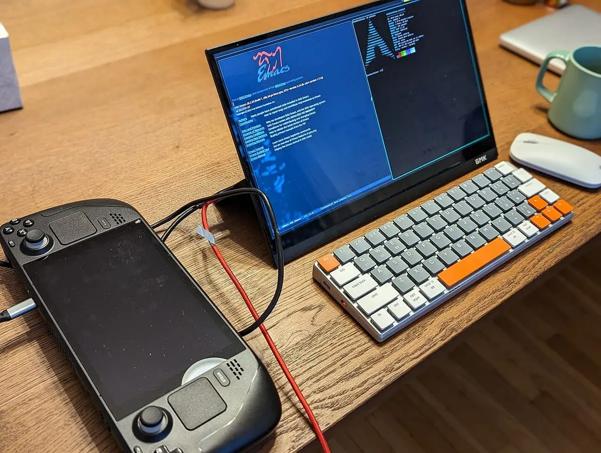 机の上の Steam Deck。ケーブルで外部モニターとキーボードにつながり、モニターには Linux のデスクトップが映っている