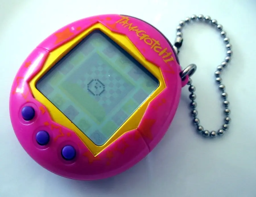 A pink Tamagotchi on a ball chain, with three buttons and an LCD screen in its egg-shaped body (photographed in 2005)