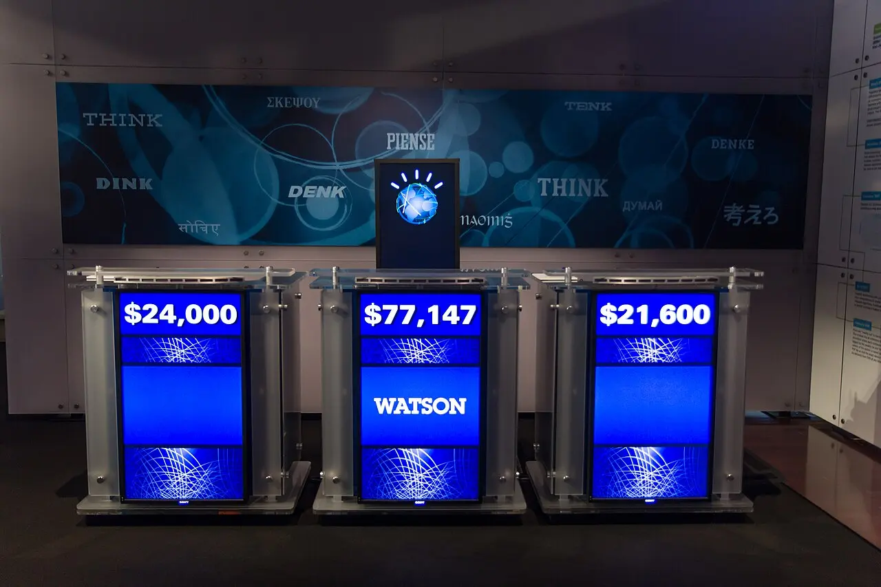 Jeopardy! 対戦の解答席の再現展示。中央の Watson の席に7万7147ドル、左右の席に2万4000ドルと2万1600ドルが表示されている