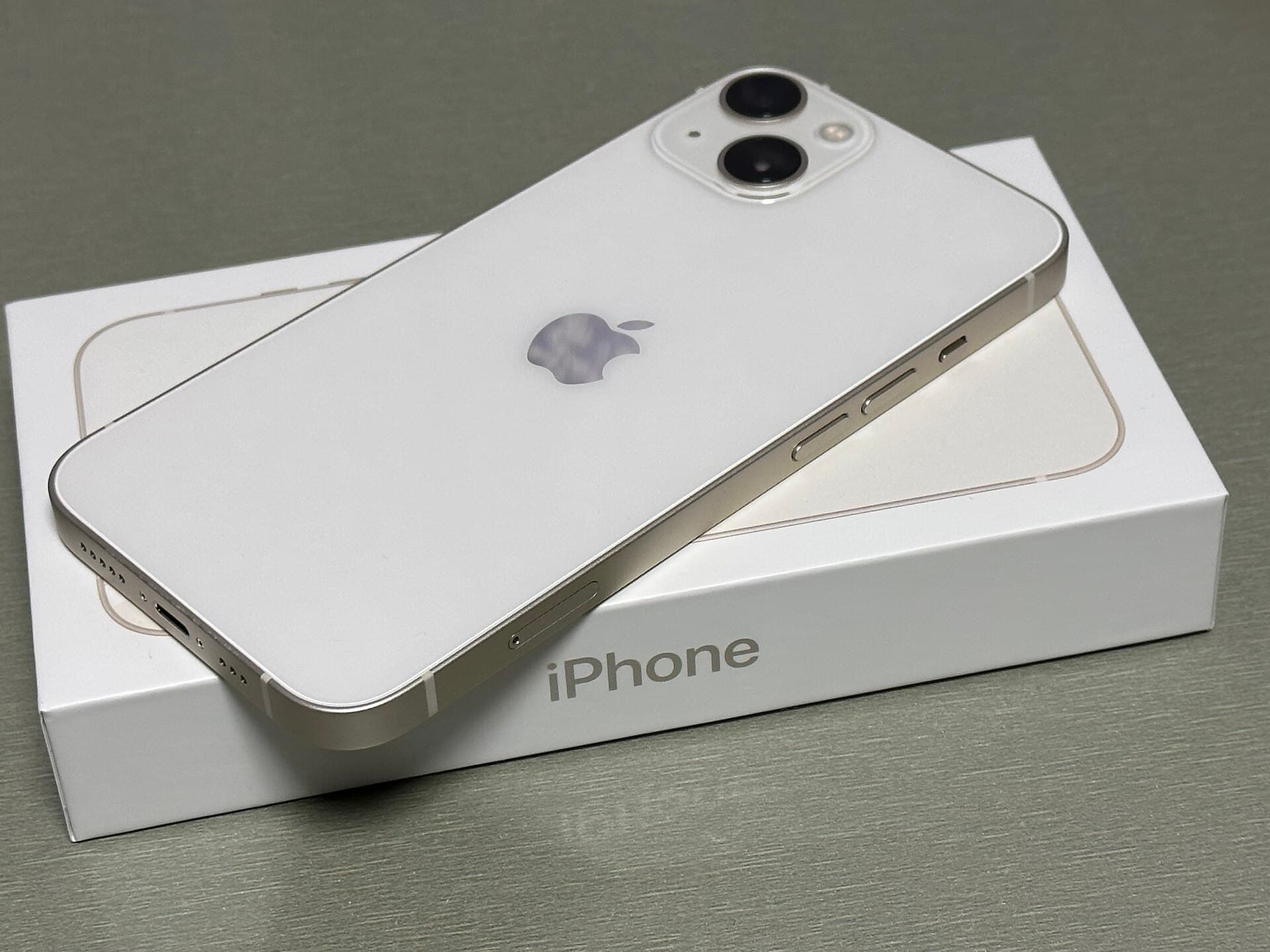 The back of a starlight iPhone 13 resting at an angle on its white retail box, showing the two rear cameras set diagonally