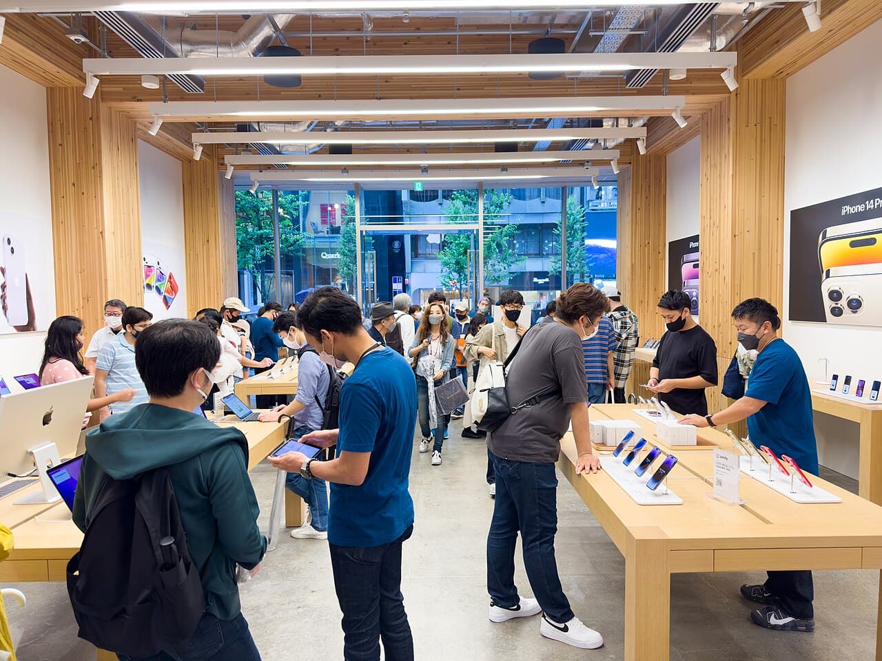 Apple Store Ginza, Tokyo, days after launch: an iPhone 14 Pro poster on the right-hand wall and customers around tables of demo units