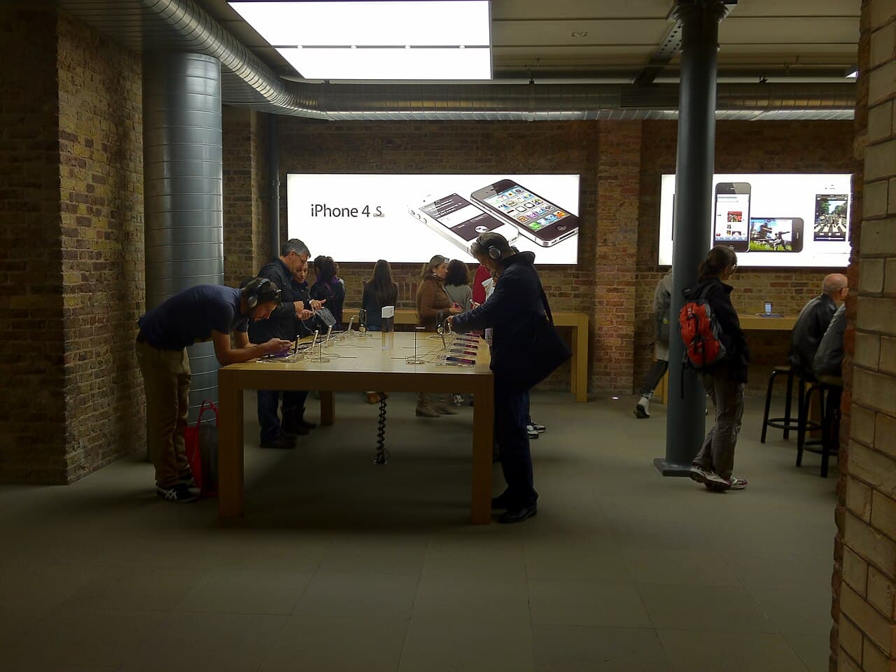 Customers trying iPhone 4S demo units in an Apple Store days after launch, with the iPhone 4S display wall behind them