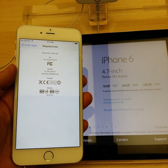 An iPhone 6 demo unit held in an Apple Store on launch day, with the in-store panel behind it listing the 16GB, 64GB and 128GB prices