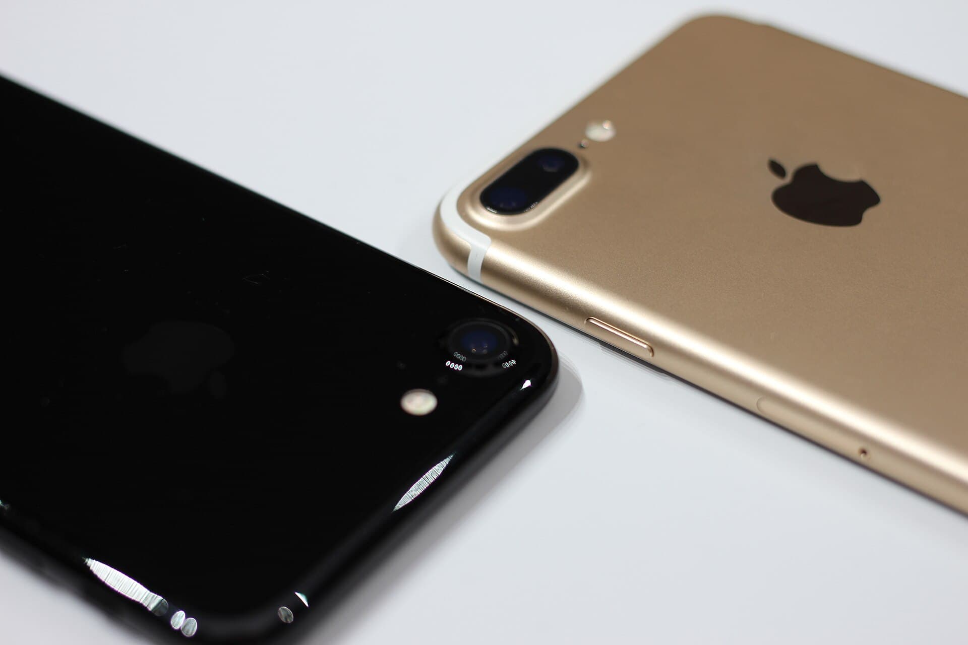 Close-up of the backs of a jet-black iPhone 7 (left) and a gold iPhone 7 Plus (right), the Plus carrying its two rear cameras