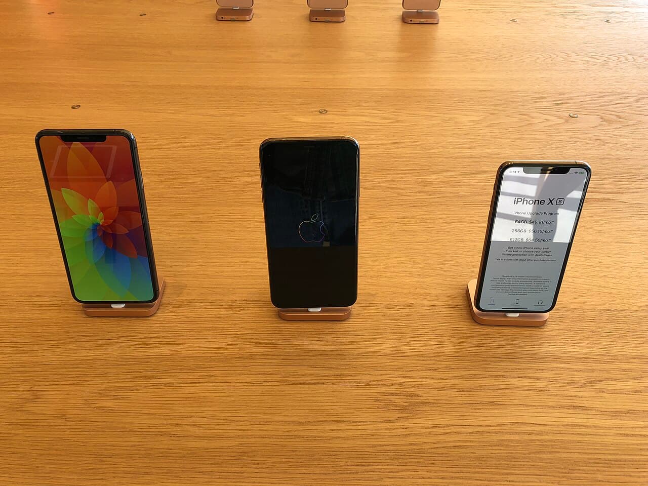 Three notched iPhone XS units on display on a wooden Apple Store table